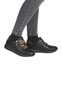 Black leather sneakers feature a textured finish, brown laces, a side zipper, and a low-profile rubber sole with a gold accent line.