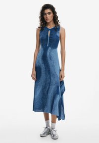 Blue sleeveless dress with a keyhole neck detail, featuring a textured wave pattern, asymmetrical hem, and lightweight fabric.