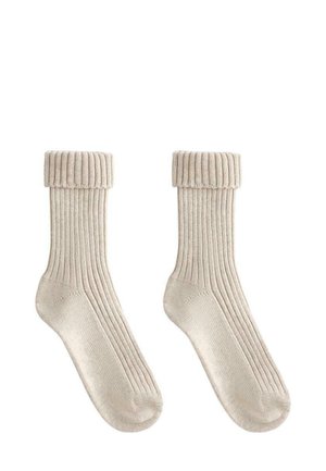 Et par beige ribbede strikkede sokker med foldede manchetter, vist fladt mod en hvid baggrund.