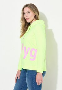 Helder neonkleurige groene hoodie met roze letters, lange mouwen, verstelbare capuchon en een ontspannen pasvorm. Gladde stoftextuur en casual ontwerp.