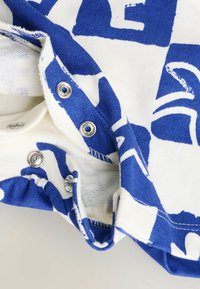 Blau-weißer Baumwollstoff mit einem bedruckten Muster und silbernen Druckknöpfen. Verfügt über rohe Kanten und eine weiche Textur.
