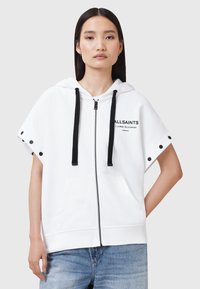 Sudadera blanca de manga corta, con cordones negros y botones laterales. Cuenta con un cierre frontal y un bolsillo canguro, con un logo impreso en el pecho.