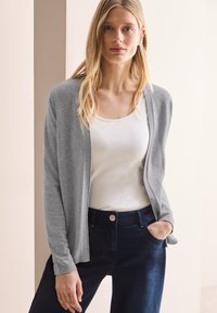 Grauer Cardigan mit offener Front, langen Ärmeln und gerippten Bündchen, kombiniert mit einem weißen Tanktop und einer dunkelblauen Hose. Glatte Textur, leichtes Design.