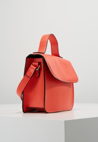 Sac à main de couleur corail avec un design structuré, une texture lisse, une poignée supérieure, une bandoulière amovible et un accent noir sur les bords.