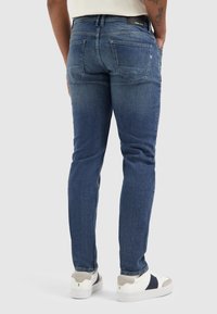 Blauwe denim jeans met een slim fit, middelhoge taille en achterzakken, gecombineerd met witte sneakers met grijze en marineblauwe accenten.