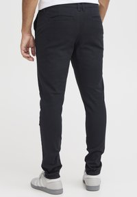 Slim-fit svarta byxor av slät tyg med två bakfickor, i kombination med ljusgrå sneakers med vita accenter.
