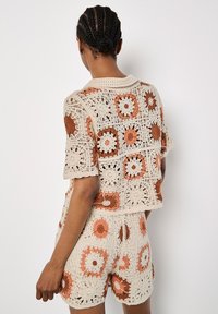 Häkeloberteil und Shorts-Set in Creme mit orangefarbenen Blumenmotiven. Verfügt über eine offene Gewebestruktur und kurze Ärmel mit lockerer Passform.