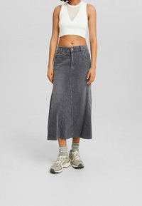 Falda midi de mezclilla gris con detalles de costura en el frente, bolsillos laterales y un dobladillo sin acabar. Combinada con un top corto blanco y zapatillas grises.