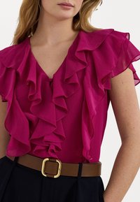 Fuchsia blouse with ruffled sleeves and a V-neckline. Paired with a brown belt featuring a square gold buckle. Black skirt visible.