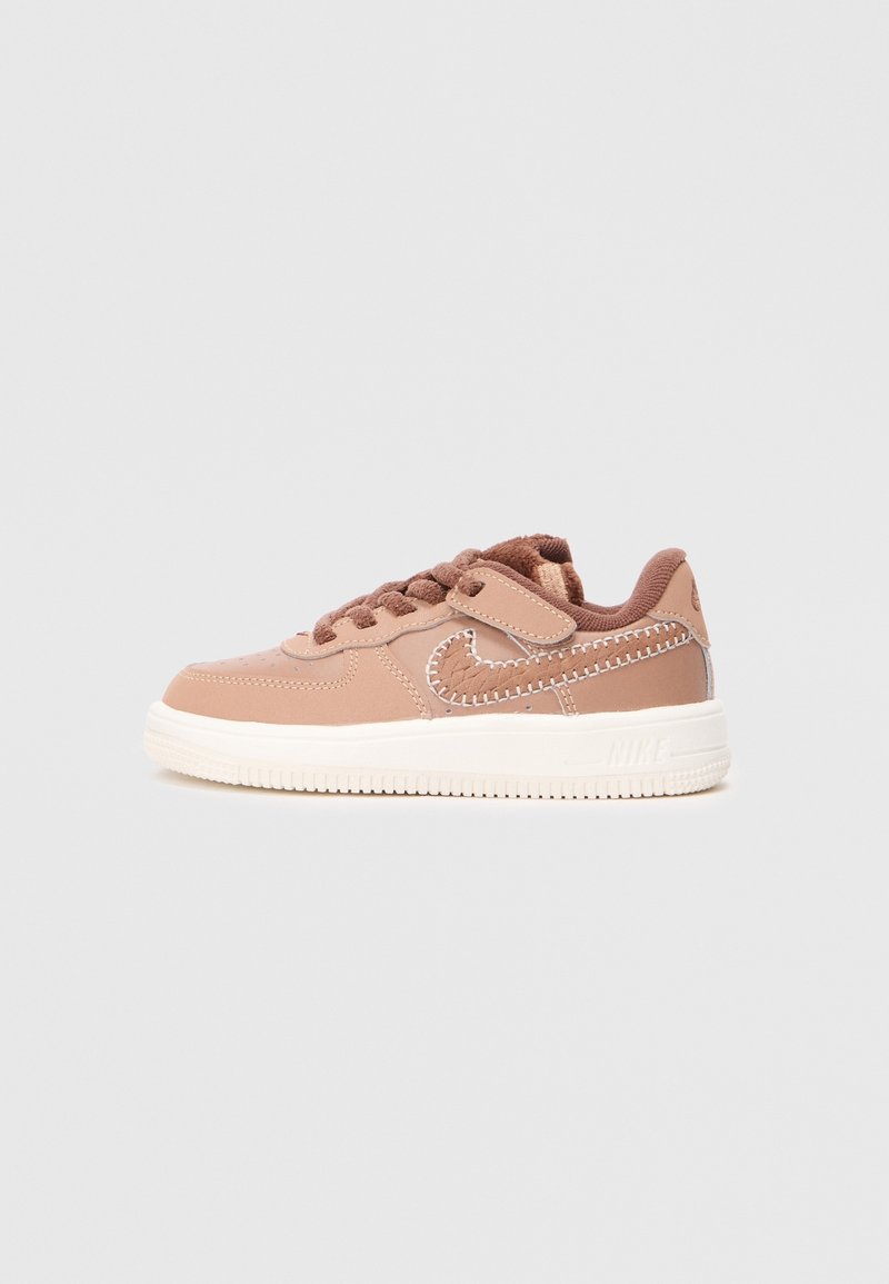 Baskets marron taille enfant avec semelle blanche, bride Velcro et logo Nike swoosh cousu sur un fond gris uni.