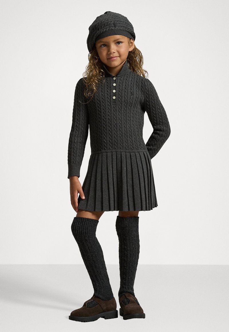 Adīta tumši pelēka kleita ar ribotu tekstūru, pogām aizdara apļa apkakli, plīša svārki, apvienota ar ceļgala auguma ribotām zeķēm un brūnām kurpēm.