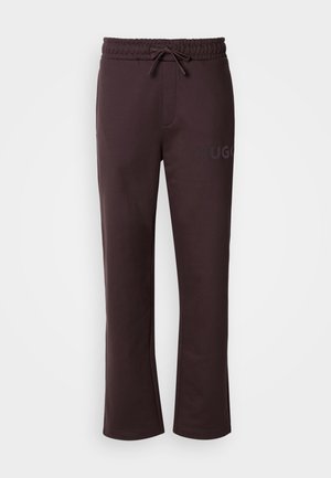 Sötétbarna melegítőnadrág elasztikus derékpánttal, húzózsinórral, oldalzsebekkel és a bal lábszáron nyomtatott "HUGO" logóval. Puha tapintású.