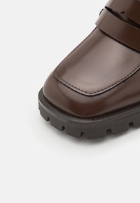 Botte en cuir marron à finition brillante, dotée d'une large sangle, d'une semelle noire robuste et d'un embout arrondi.