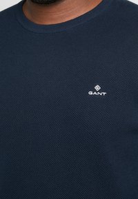 Marineblauwe gebreide trui met een ronde hals en een klein wit GANT-logo op de borst. Zachte, ademende stof.