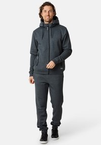 Mörkgrå zip-up hoodie med huva, kängurufickor och dragsnören, tillsammans med matchande joggers och svarta sneakers på en neutral bakgrund.