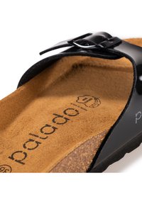 Svart lackad slidesandal med spänne, med en beige korkfotbädd och en mjuk textur. Logotyp tryckt på fotbäddens yta.