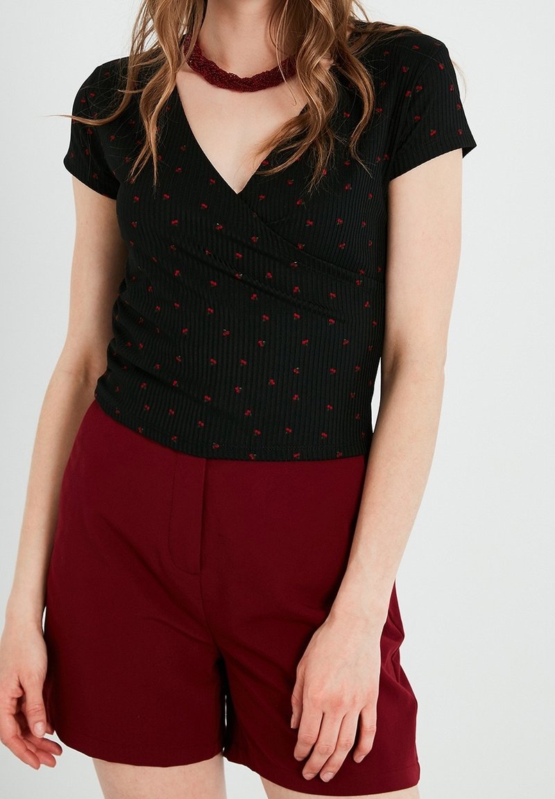 Musta ribbineuloksinen toppi, jossa V-kaula-aukko, lyhyet hihat ja punainen kukkakuvio. Yhdistetty viininpunaisiin shortseihin. Tiukasti istuva malli.