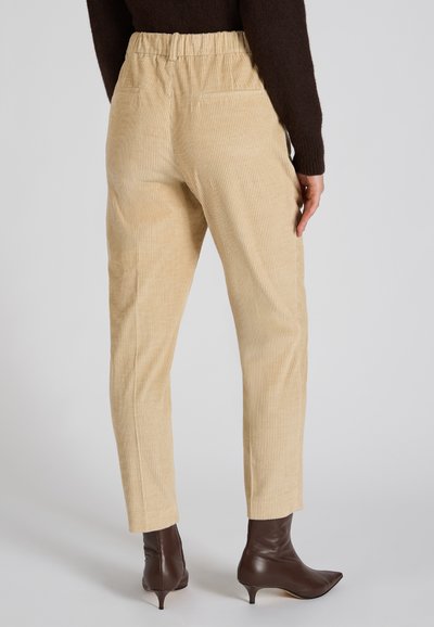 Pantalones de pana beige con un acabado texturizado, cinturilla elástica y dos bolsillos traseros, combinados con botines marrones.