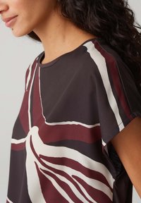 Korte mouw top in donkerbruin met een gedurfde abstracte print in bordeauxrood, wit en blauw. Zachte stof met een gladde textuur en een losse pasvorm.