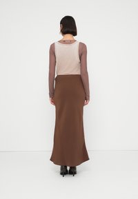 Jupe longue marron à la texture lisse, associée à un haut ajusté à manches longues de couleur beige clair, avec un léger décolleté dos arrondi.