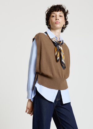 Gilet marrone lavorato a maglia sopra una camicia azzurro chiaro, accentuato da una sciarpa a righe nere e gialle. Pantaloni blu navy, hardware minimo, design casual.