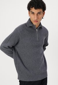 Grauer gerippter Pullover mit hohem Kragen und halbem Reißverschluss. Hergestellt aus einem strukturierten Strickstoff. Gerade Passform mit langen Ärmeln.
