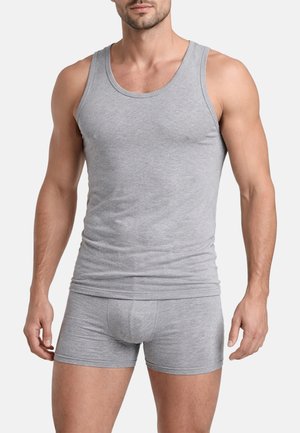 Uomo che indossa una canottiera grigia aderente e boxer grigi abbinati, in piedi davanti a uno sfondo bianco semplice.