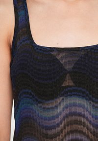 Must mustekate, millel on ruudukujuline kaelus ja tekstuuriga kudum, mis sisaldab erinevaid sinise ja musta toone, luues lainelaadse efekti.