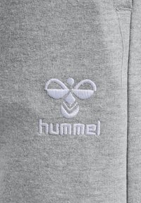 Graue Sweatpants aus einem weichen Stoff mit einem weißen gestickten Logo und einem Bienenmotiv am linken Bein. Einfaches Design, lässiger Stil.