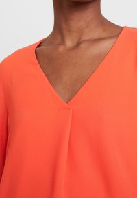 Top naranja de cuello en V hecho de una tela ligera, con un diseño limpio y un sutil detalle de costura en el escote.