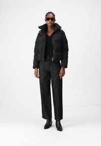 Black quilted puffer jacket with a high collar, paired with dark denim wide-leg pants and black ankle boots. Sunglasses complete the look.
