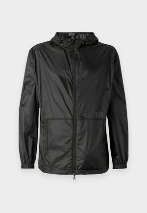 Veste légère noire avec capuche, dotée d'une fermeture éclair sur toute la longueur, de poignets élastiques et d'une texture lisse et brillante. Logo imprimé sur le devant.