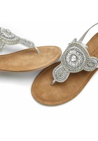 Sandales tongs en argent ornées de perles avec accents de bijoux et un semelle en suédine beige. Présente des motifs circulaires et une sangle texturée.