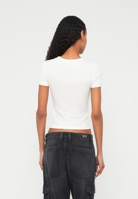 Fehér, rövid ujjú, testhez simuló póló bordázott mintával, kerek nyakkivágással, magas derekú fekete cargo nadrággal viselve, amely nagy zsebekkel rendelkezik.