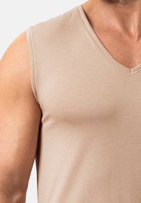 Débardeur beige sans manches avec un décolleté en V. Le tissu présente un motif texturé, mettant en valeur une matière lisse et légère.