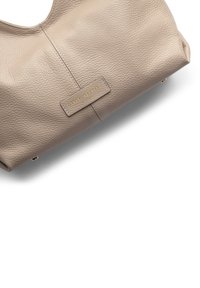 Beige leather handbag with a textured finish, featuring a central seam and a gold embossed logo plate on the front.