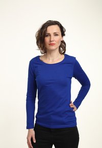 Camisa azul de manga larga hecha de tela suave con cuello redondo, combinada con pantalones oscuros, presentada sobre un fondo claro.