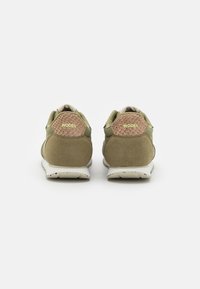 Sneakers verde in suede e rete con un tallone marrone texturizzato e la scritta dorata "WODEN", caratterizzati da una suola bianca chiazzata.