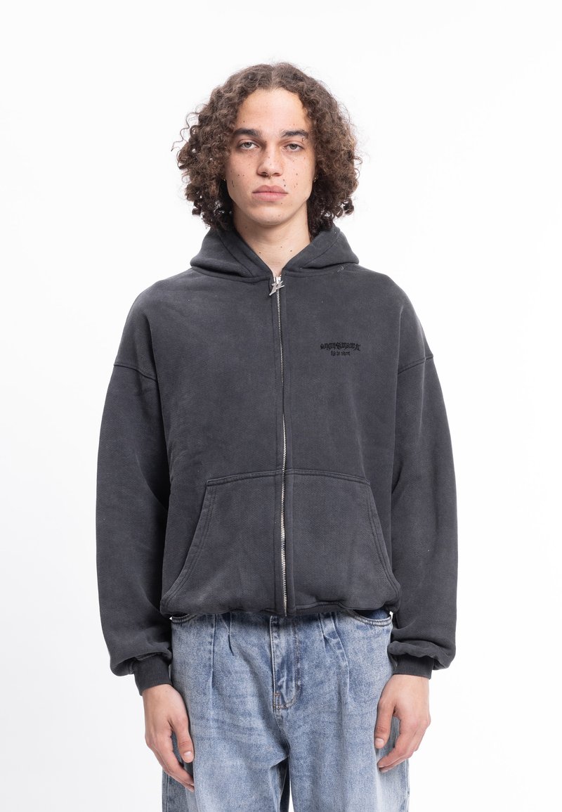 Černá mikina na zip z měkké látky s klokaní kapsou. Má kapuci a nenápadné logo na hrudi. Nositelná s světle modrými džínami.