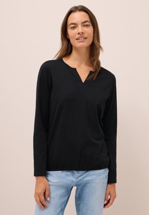 Haut noir à manches longues avec un décolleté en V et un subtil détail de couture. Matière douce, coupe décontractée, porté avec un jean bleu clair.