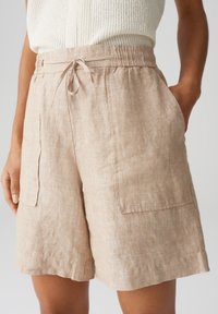 Pantaloni corti in lino beige con vita elastica e cordoncino regolabile, dotati di due tasche frontali e una vestibilità comoda.