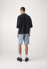 Čierne oversized tričko, denimové šortky, čierne topánky, biele ponožky. Jednoduchý dizajn, uvoľnený strih, krátke rukávy a jemný detail zadného švu.
