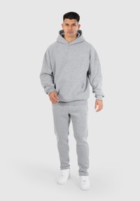 Haut à capuche gris clair et pantalon de survêtement assorti, en tissu doux, avec une poche kangourou et des poignets côtelés, associé à des baskets blanches.