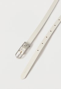 Λευκή δερμάτινη ζώνη με ασημένια πόρπη που διαθέτει γεωμετρικό μοτίβο με ανοίγματα, παρουσιάζεται σε λευκό φόντο.