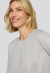 Light gray sweater with a round neckline and subtle texture. Features gentle pleating at the front and short, slightly rolled sleeves.