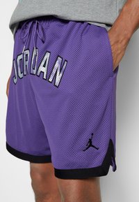 Purple mesh shorts with "JORDAN" printed in reflective silver. Features a black trim on the hem and a black Jumpman logo on the side.