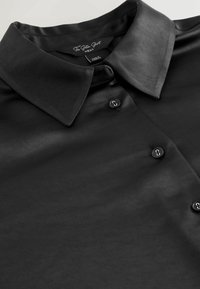 Sort satin skjorte med klassisk krave, fem knapper og glat tekstur, med et mærke der angiver størrelse og brand.