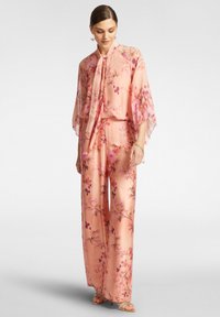 Completo floreale rosa fluido composto da una blusa con maniche a cappotto larghe e collo legato, abbinata a pantaloni a gamba larga. Tessuto morbido con dettagli di stampa floreale vivace.
