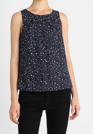 Blouse sans manches bleu marine avec petits motifs floraux blancs et roses portée avec un pantalon noir.