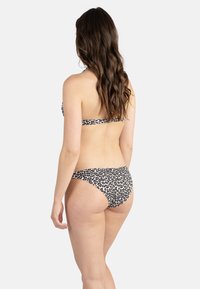 Bikini à imprimé léopard avec un col halter et des bas à couverture modérée. Fabriqué en tissu extensible, avec des couleurs noir, marron et blanc.